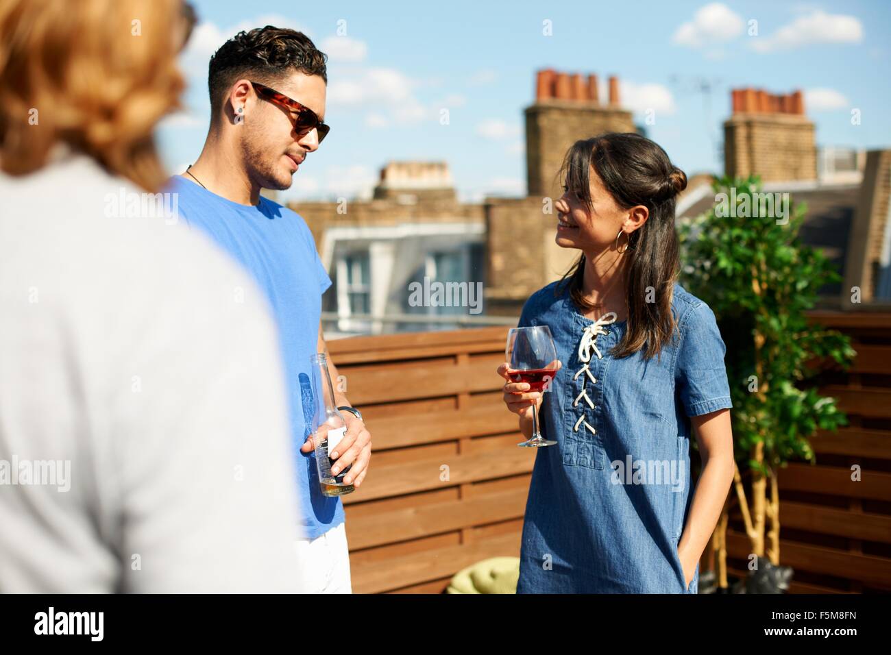 Male and female friends chatting and drinking at rooftop  party Stock Photo