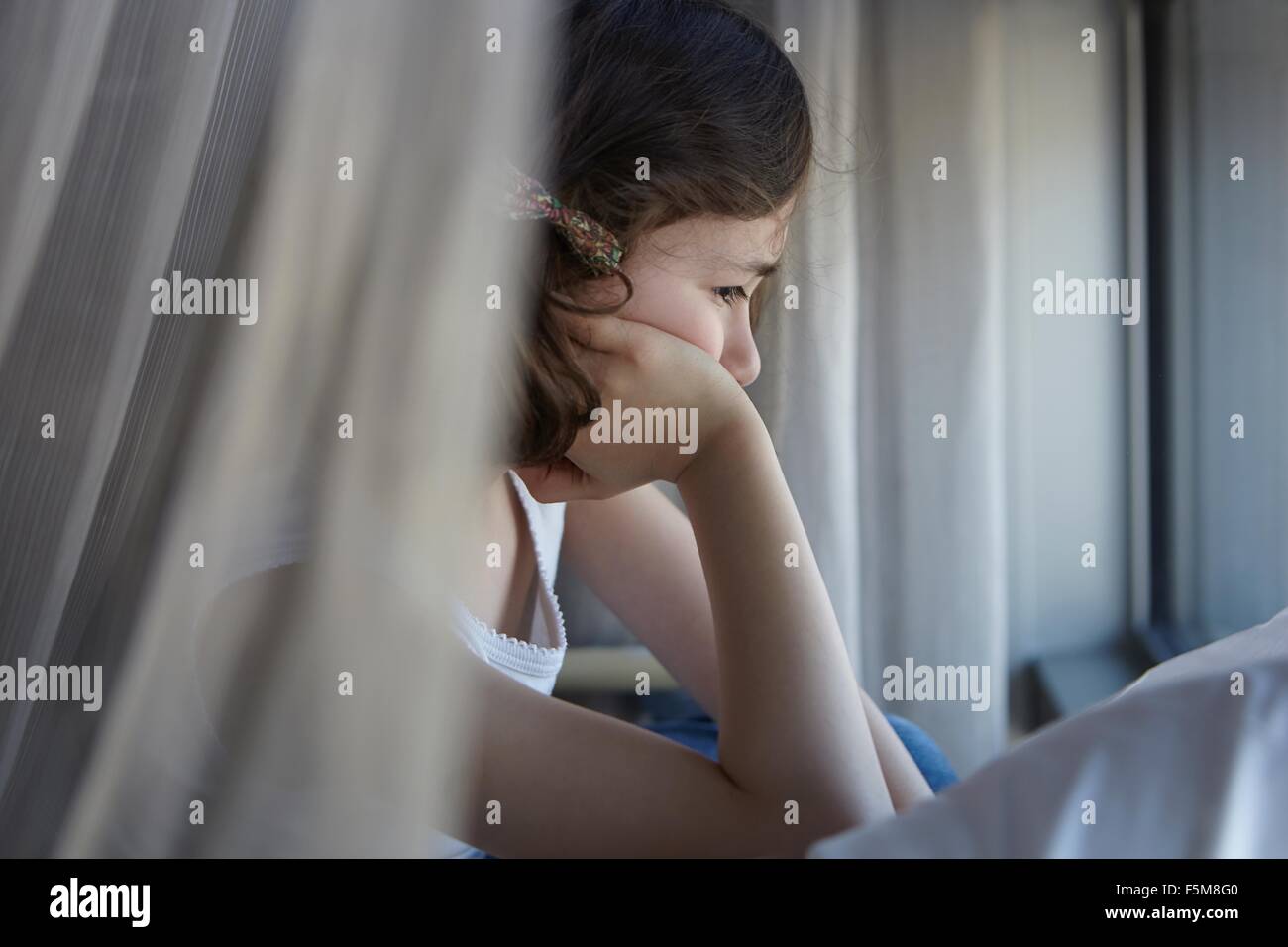 Sullen girl reclining on bed resting on elbow Stock Photo