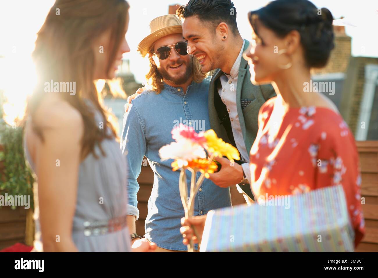 Friends at party on roof terrace holding flowers and gift smiling Stock Photo