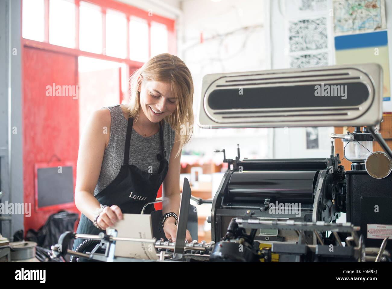 Young woman working with traditional letterpress print machine in workshop Stock Photo