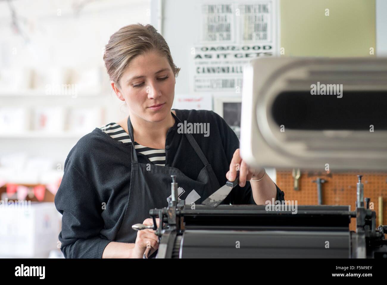 Female letterpress printer inking machine in workshop Stock Photo