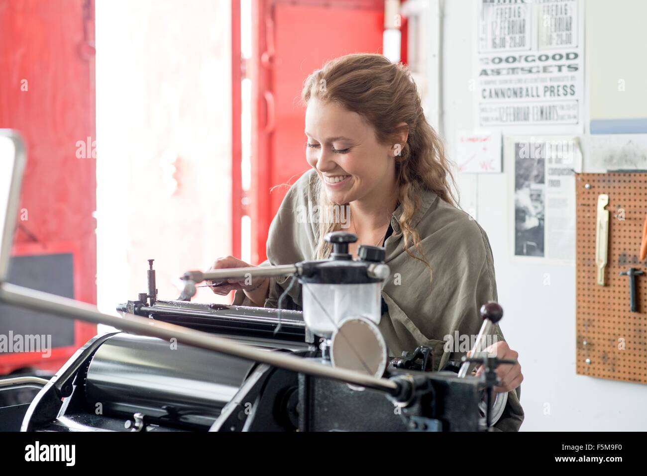 Female letterpress printer preparing printing machine in workshop Stock Photo