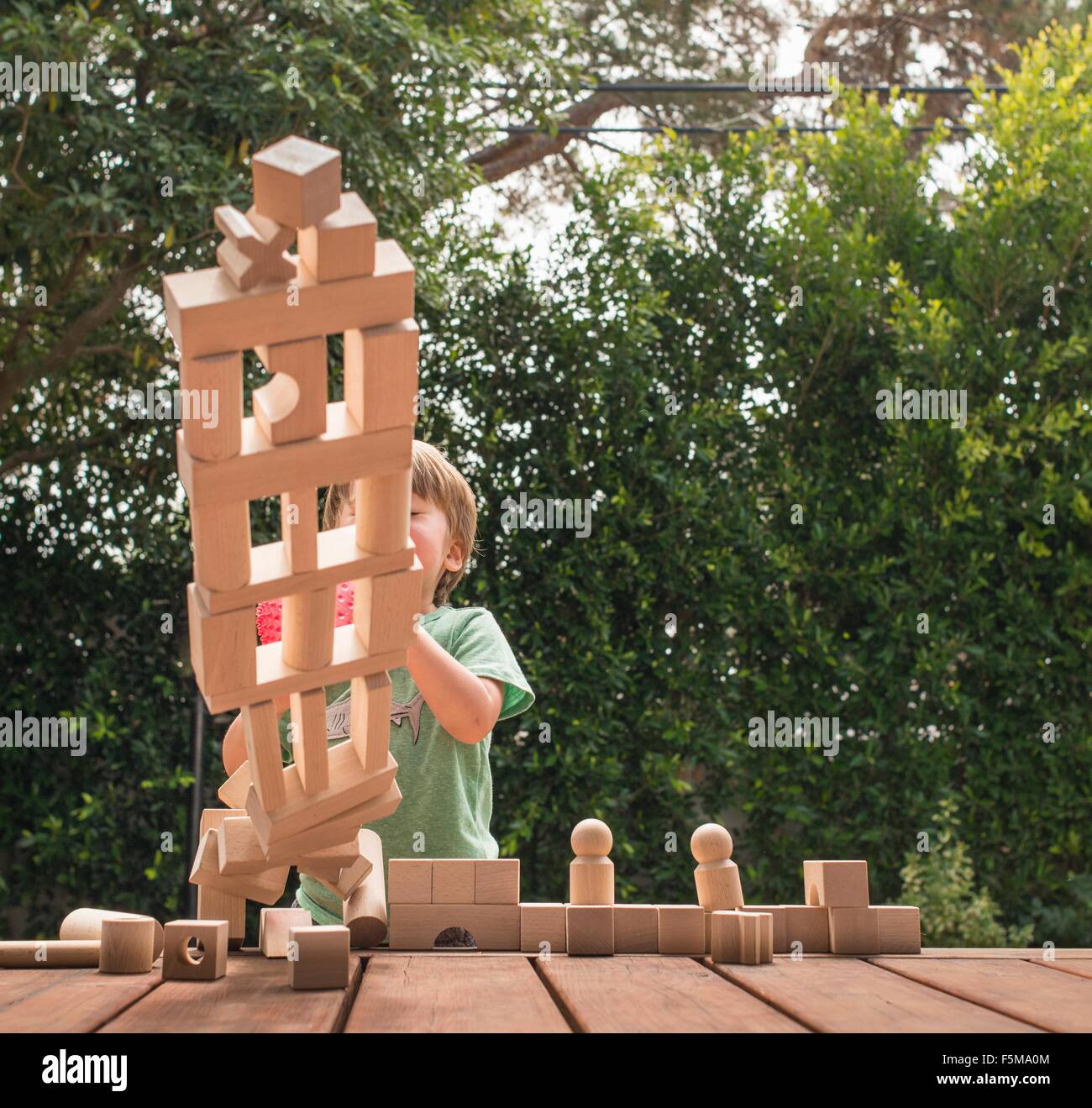 Young boy pushing over wooden structure made from building blocks, outdoors Stock Photo