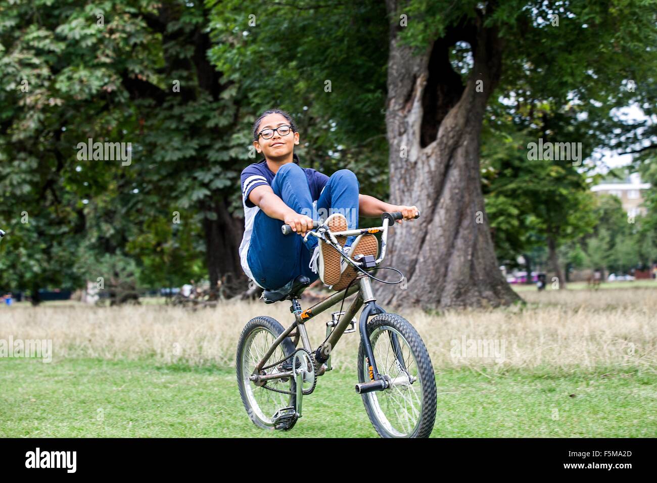 Boy riding BMX bicycle with feet up in park Stock Photo