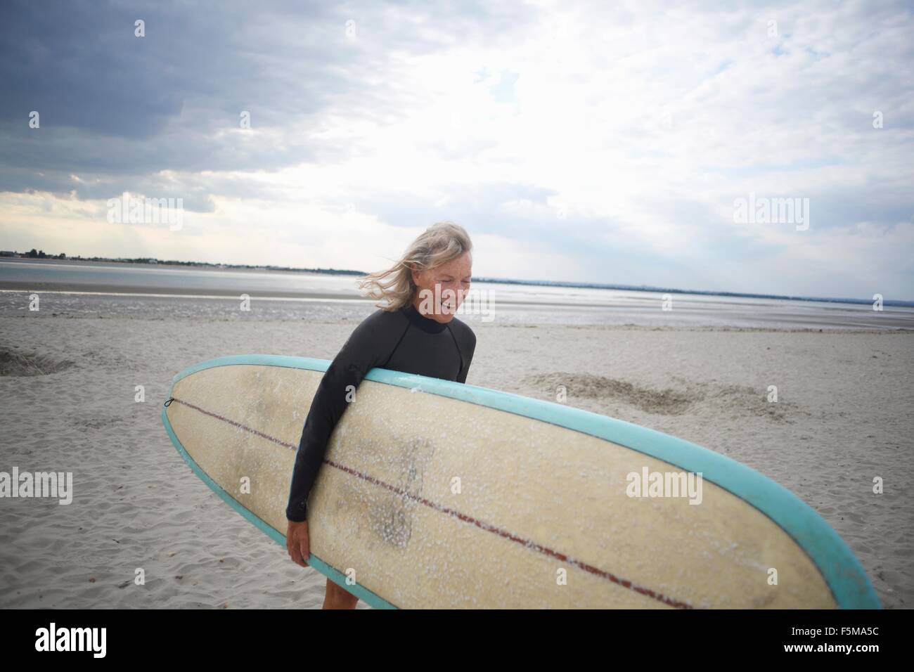 Senior woman walking from sea, carrying surfboard Stock Photo