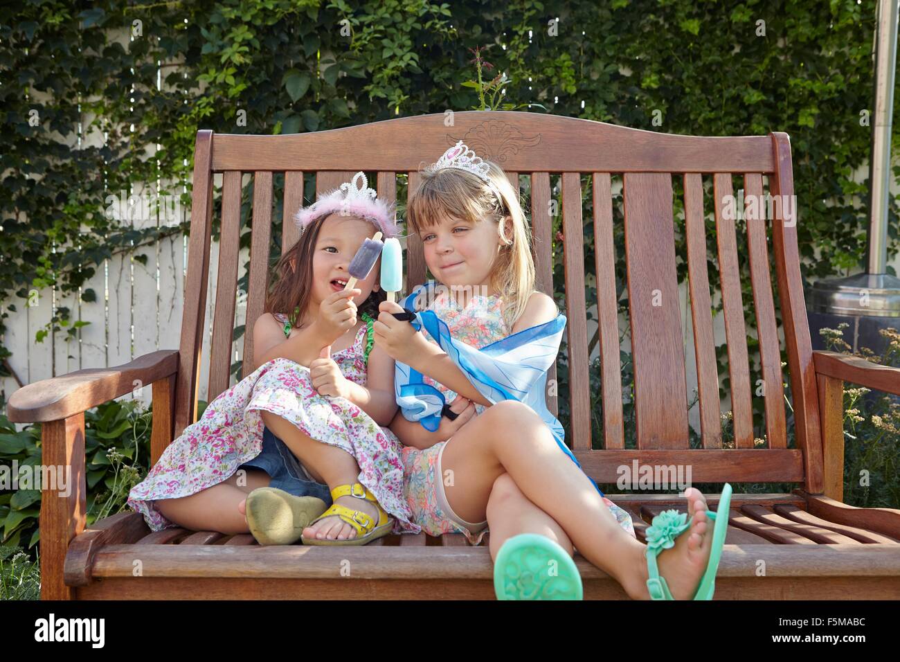 Girls enjoying ice lolly on garden bench Stock Photo