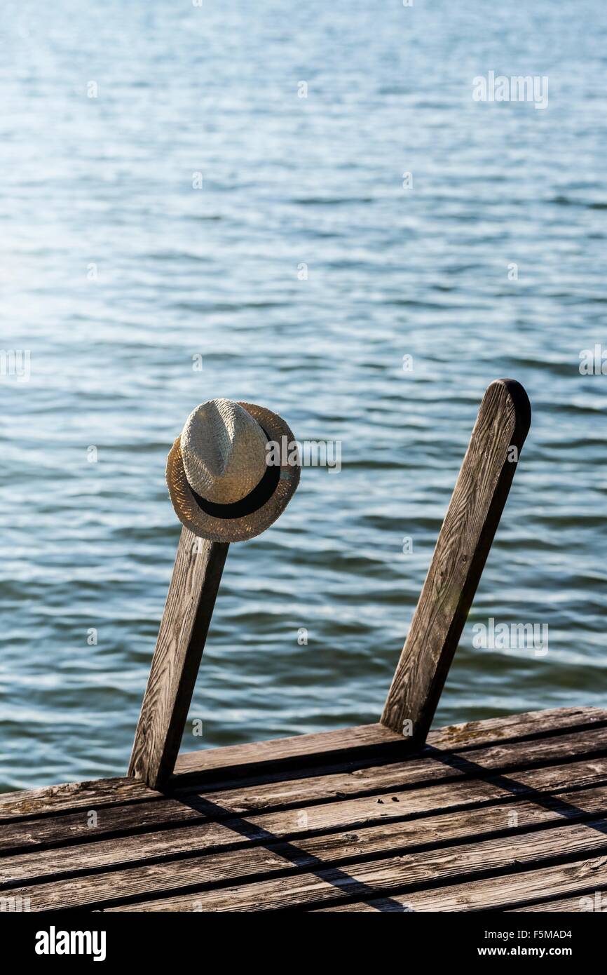 Panama hat hanging on steps of wood pier next to lake Stock Photo