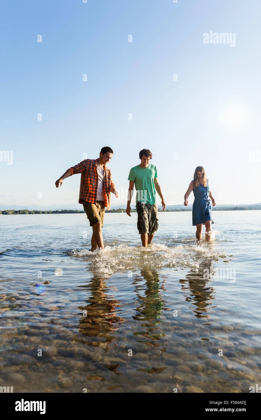 Front view of friends in a row walking ankle deep in water, Schondorf, Ammersee, Bavaria, Germany Stock Photo