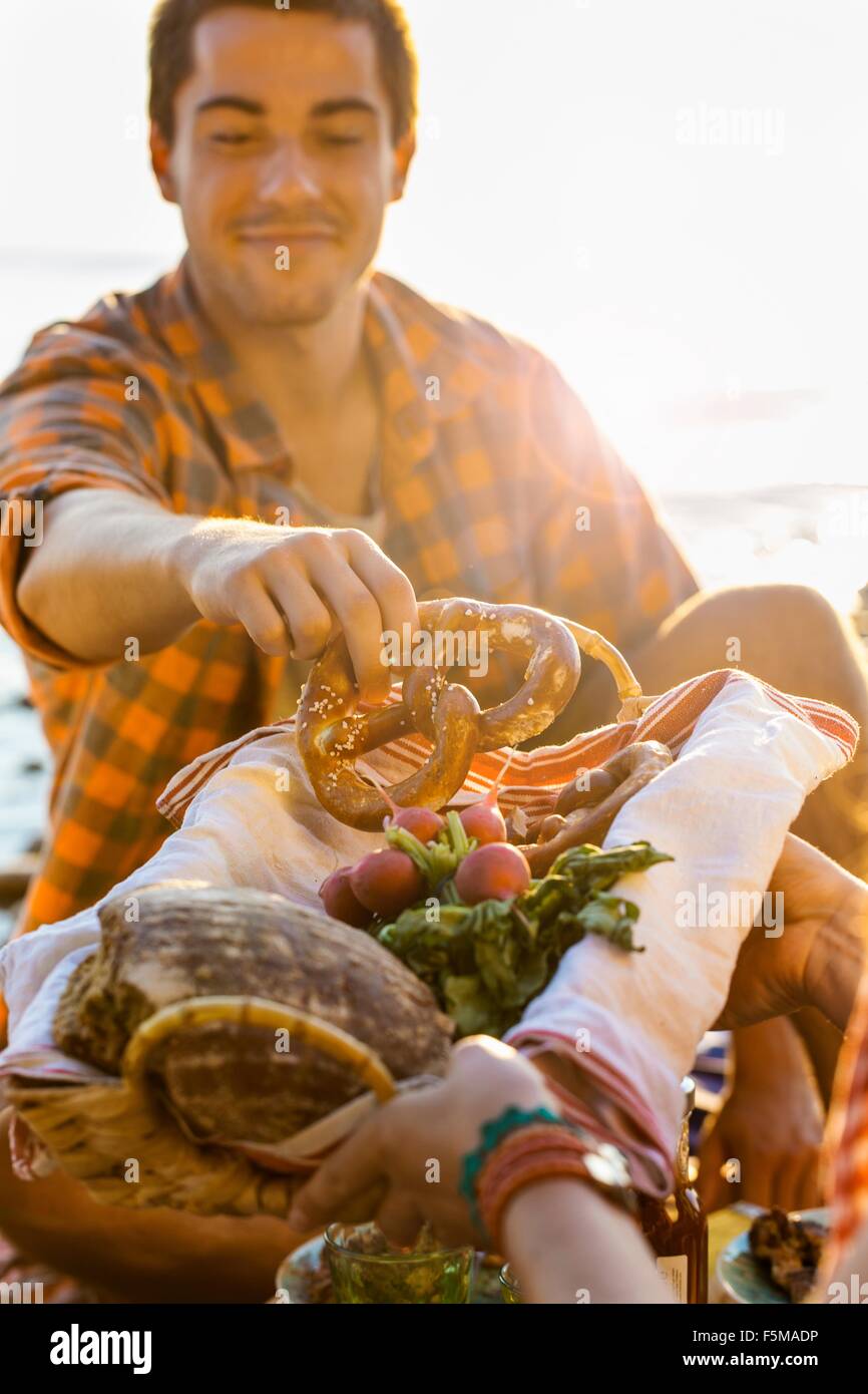 Young man accepting pretzel from bread basket, looking down smiling Stock Photo