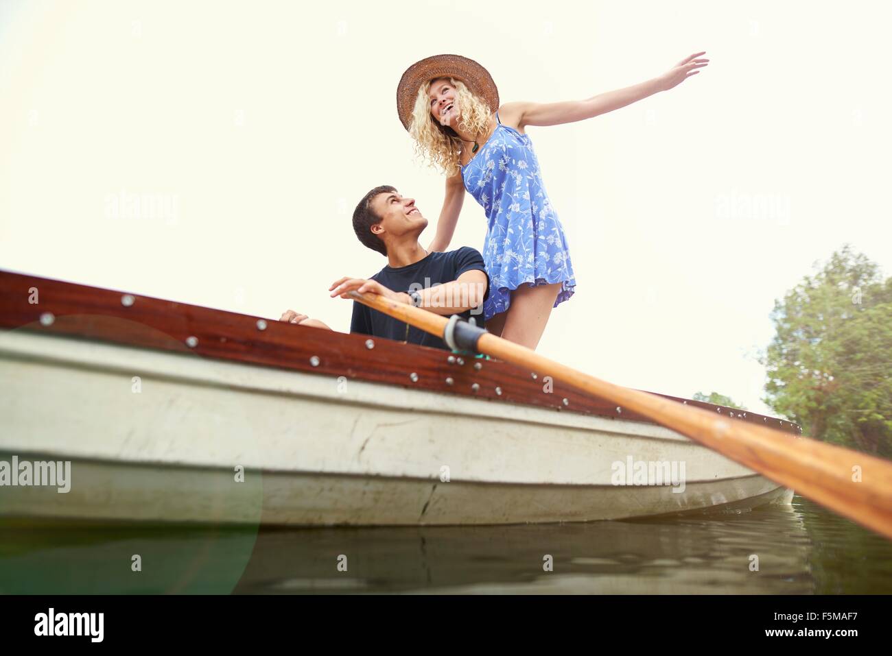 Low angle view of young woman standing in rowing boat on river Stock Photo