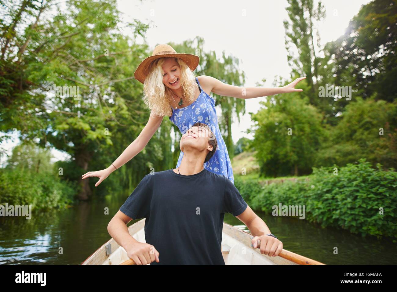 Young woman with boyfriend standing in rowing boat on river Stock Photo