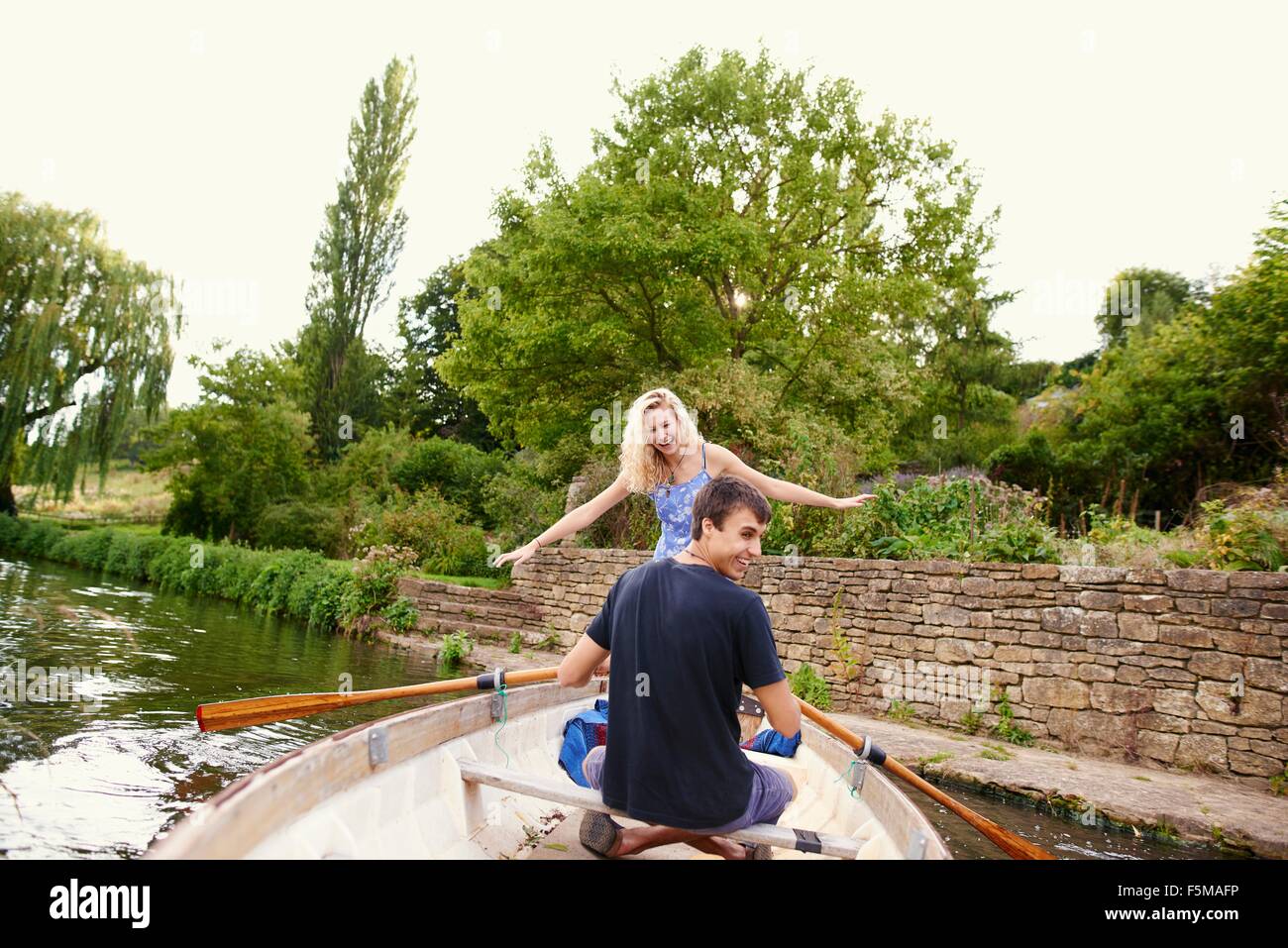Rear view of young woman with boyfriend standing in rowing boat on river Stock Photo