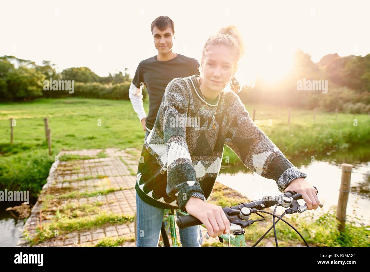 Portrait of young couple on bicycle at river footbridge Stock Photo