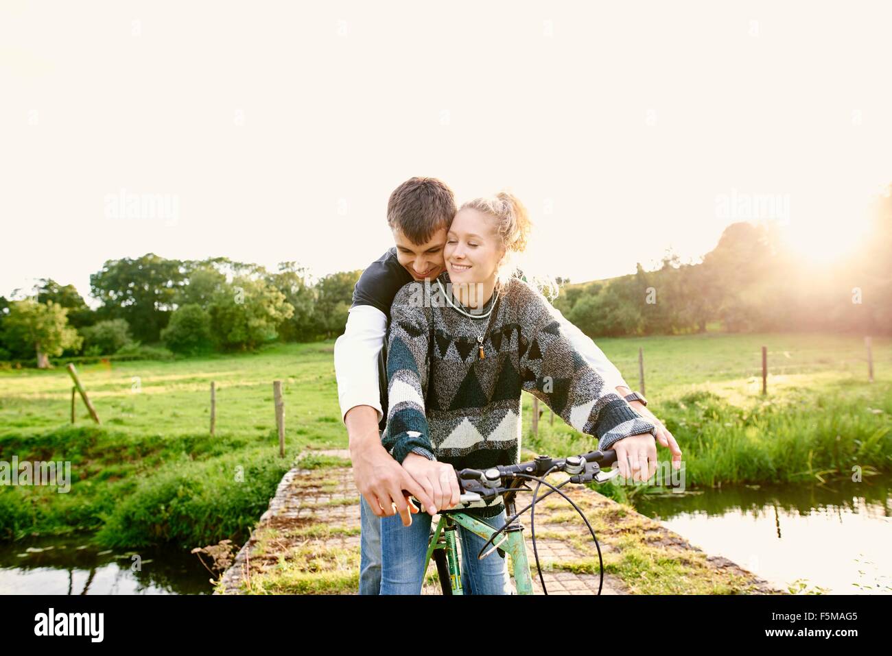 Young couple sharing bicycle at river footbridge Stock Photo