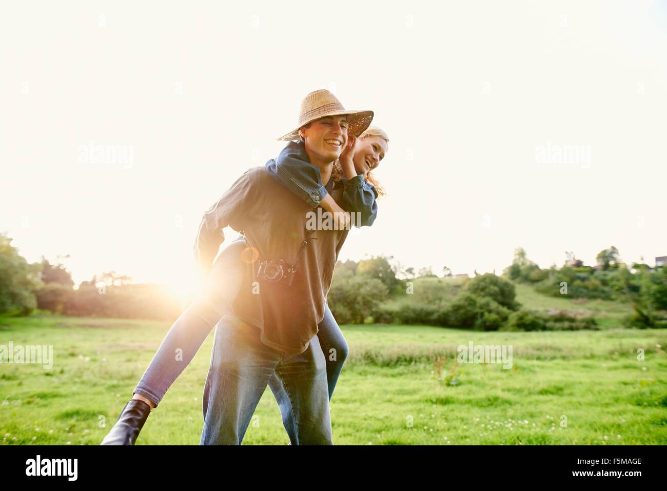 Young man giving girlfriend a piggyback in rural field Stock Photo