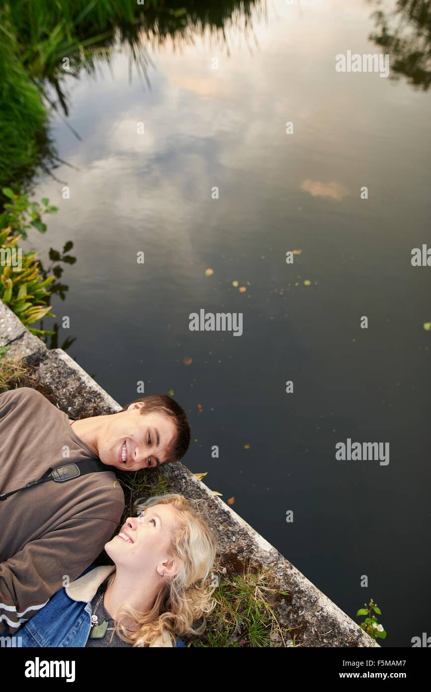 Overhead view of young couple lying on river footbridge Stock Photo