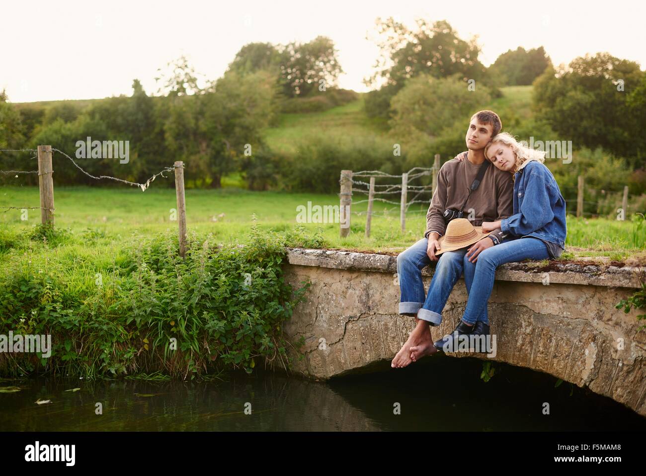 Romantic young couple sitting on river footbridge Stock Photo