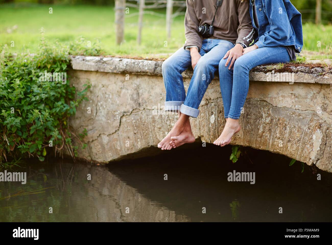 Neck down view of young couple sitting on river footbridge Stock Photo