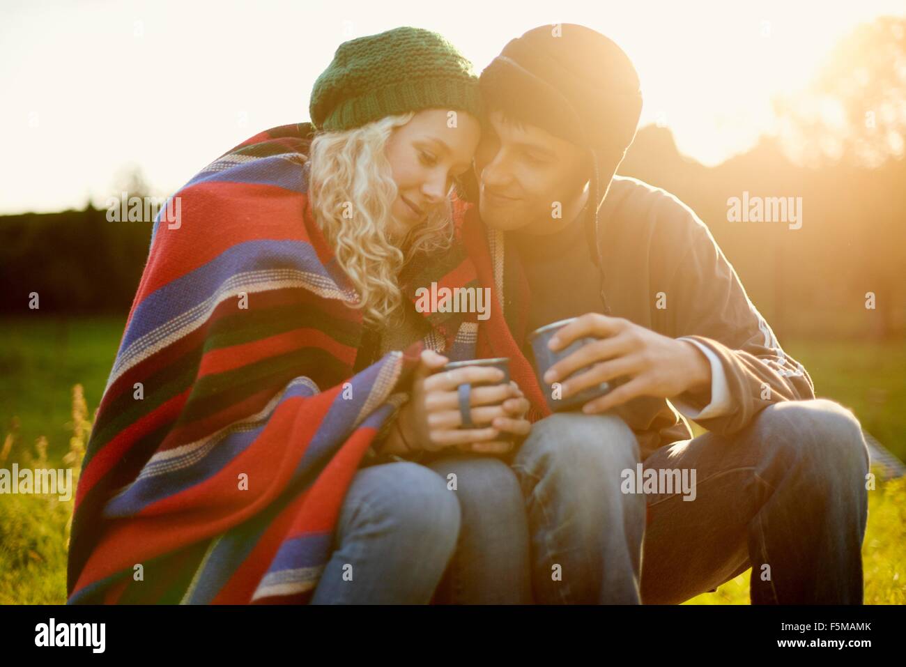 Romantic young camping couple wrapped in blanket with tea drinks Stock Photo