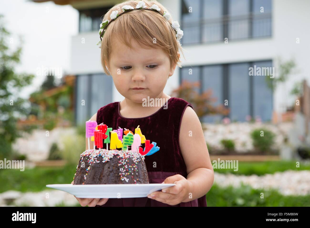 Female toddler carrying birthday cake with candles in garden Stock