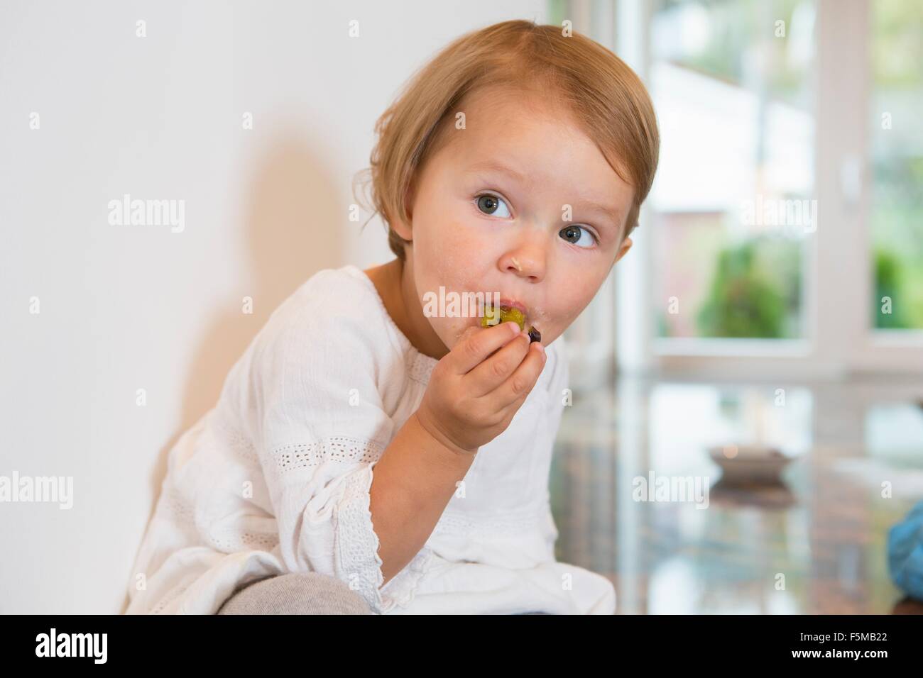 Portrait of female toddler eating plum in kitchen Stock Photo