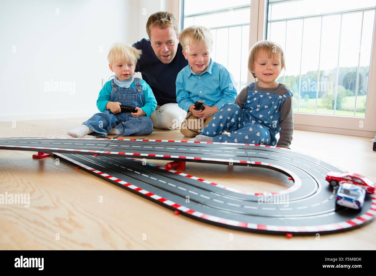 Mid adult man and three young children playing with toy  racing cars on living room floor Stock Photo