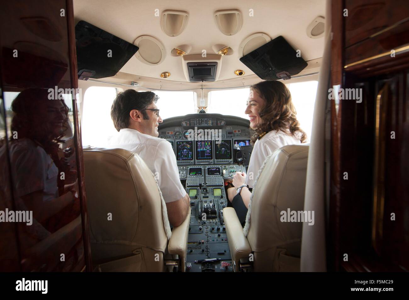 Rear view of male and female pilot chatting in cockpit of private jet Stock Photo