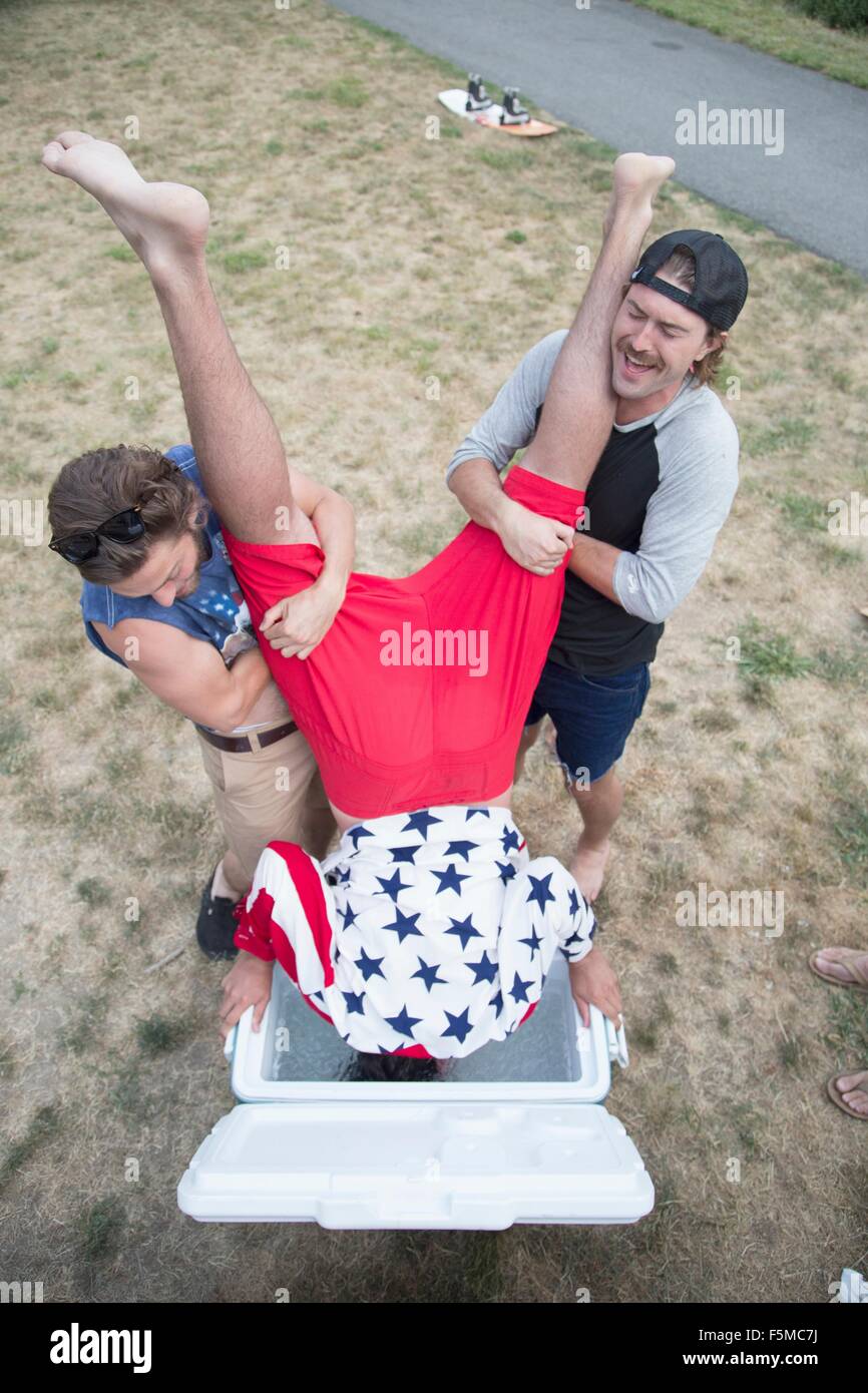 Two young men dunking friend into cooler on Independence Day, USA Stock Photo