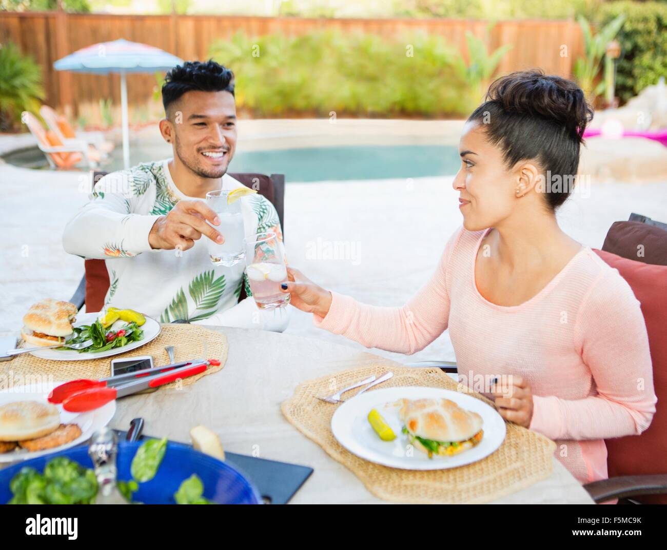 Young couple sitting down to meal outdoors making a toast Stock Photo