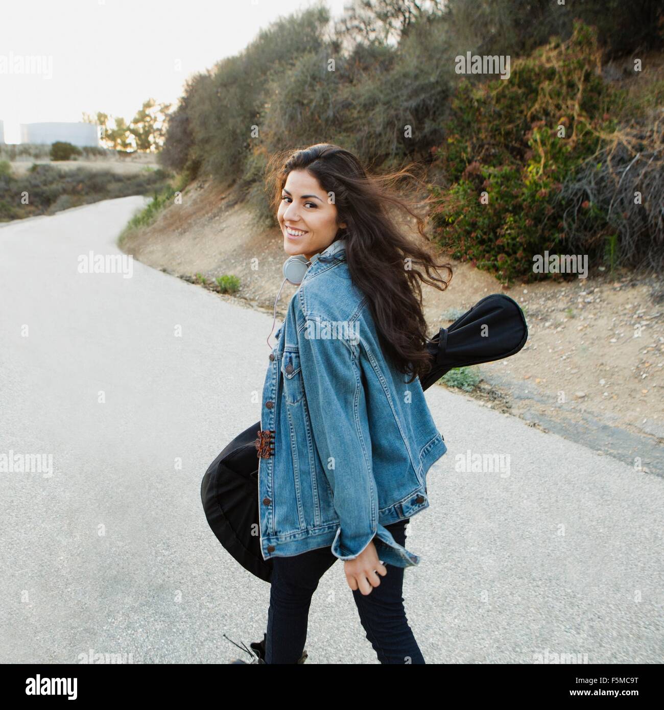 Young woman carrying guitar looking over shoulder at camera smiling, Woodland Hills, California, USA Stock Photo
