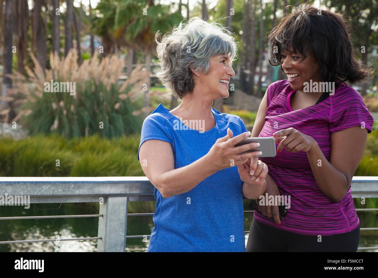 Mature female friends in park, looking at smartphone, laughing Stock Photo