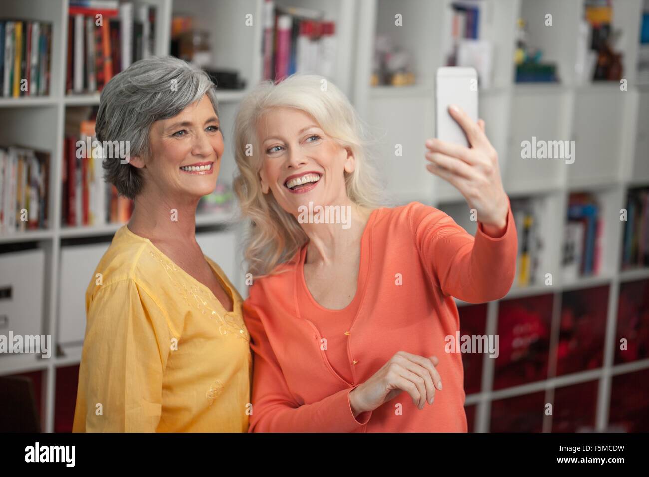 Two mature woman taking self portrait, using smartphone, indoors Stock Photo