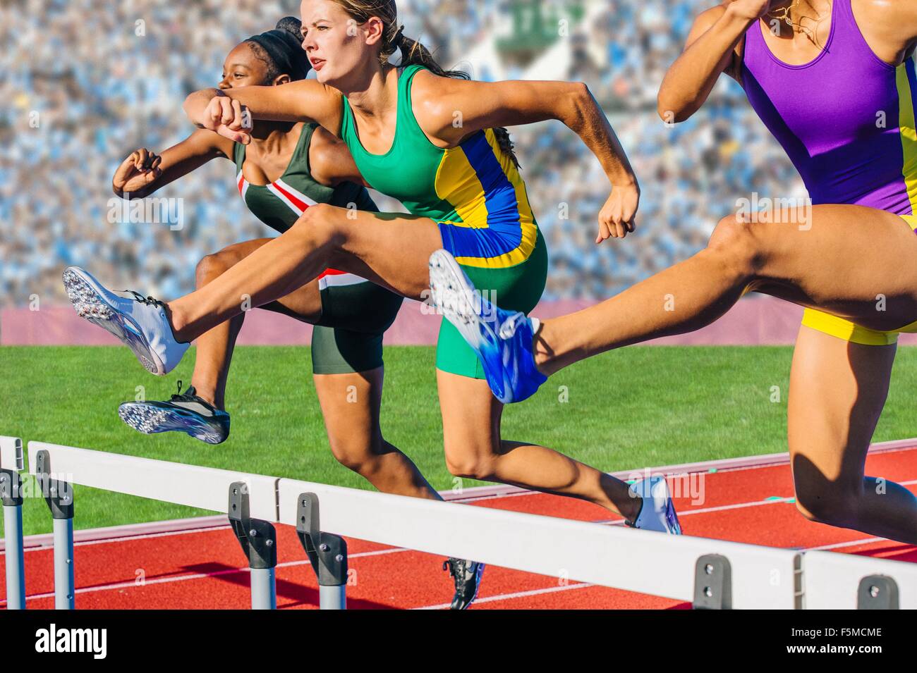Runners jumping over hurdle on track Stock Photo