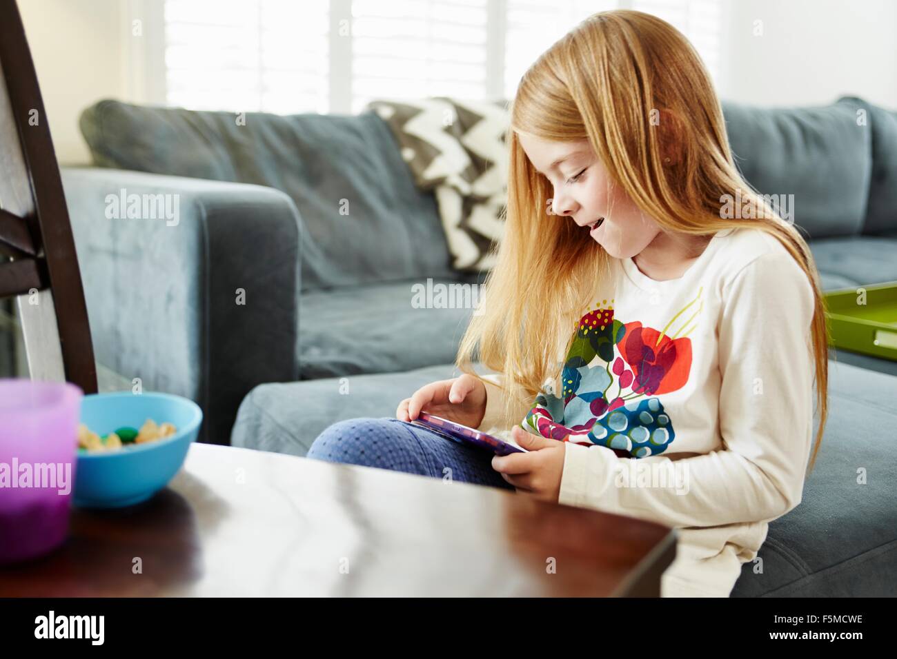 Girl using digital tablet on sofa in living room Stock Photo