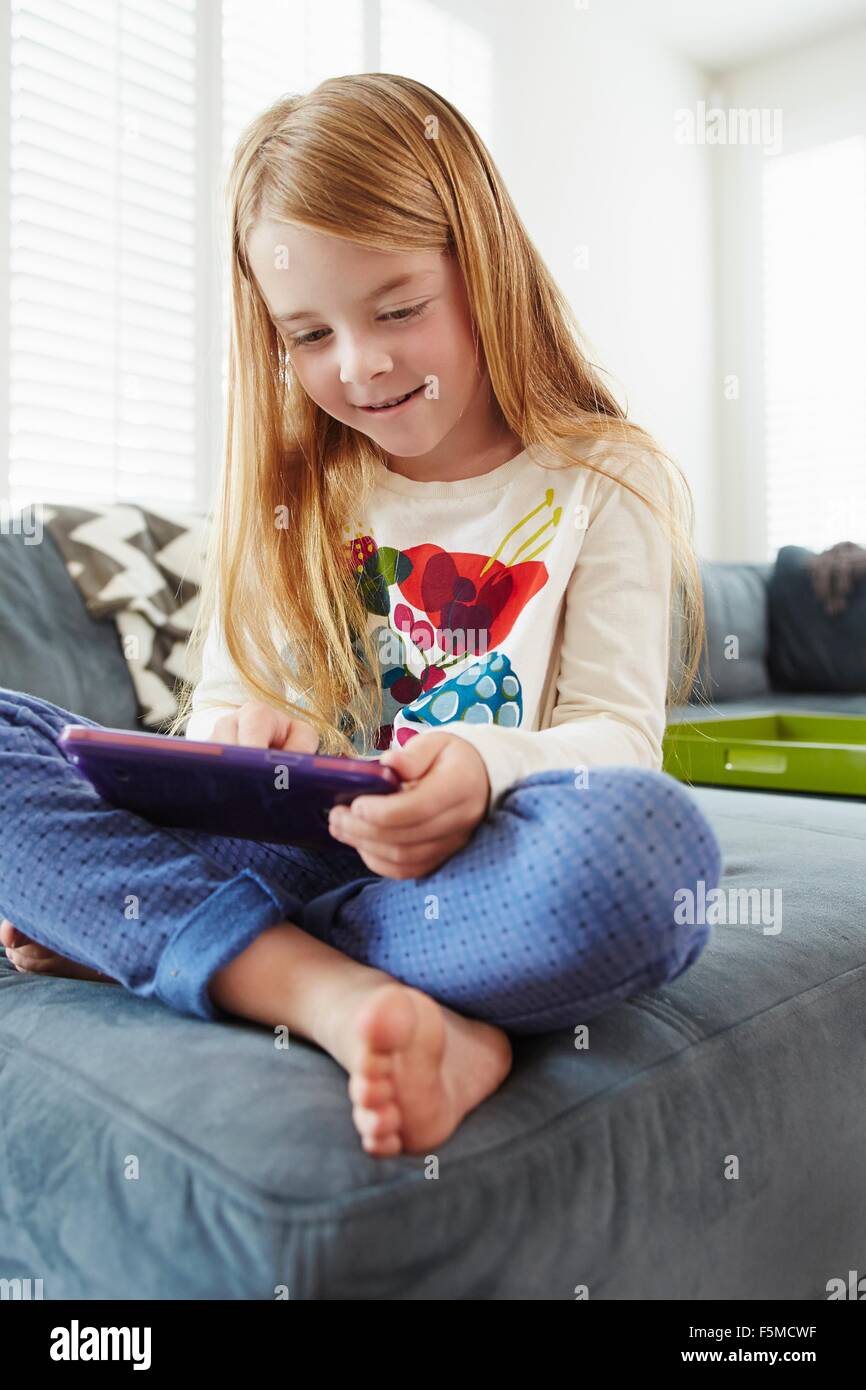 Girl using digital tablet on sofa in living room Stock Photo