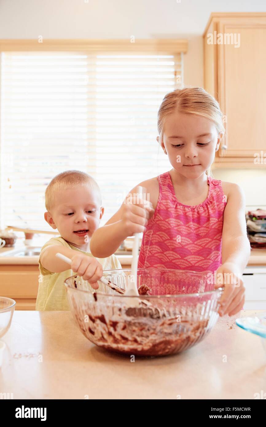 Siblings melting chocolate in mixing bowl Stock Photo