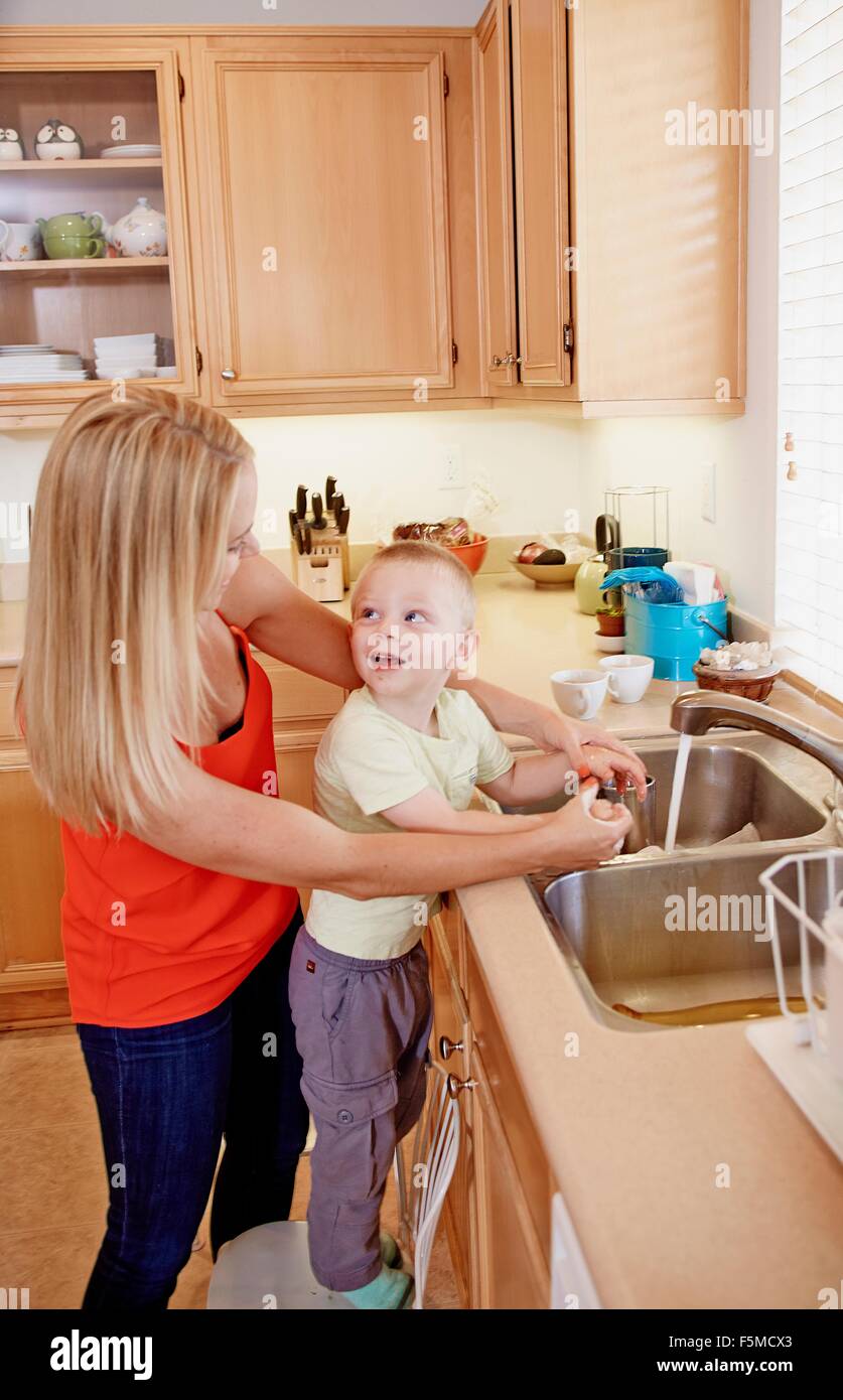 Mother washing son's hands in kitchen sink Stock Photo