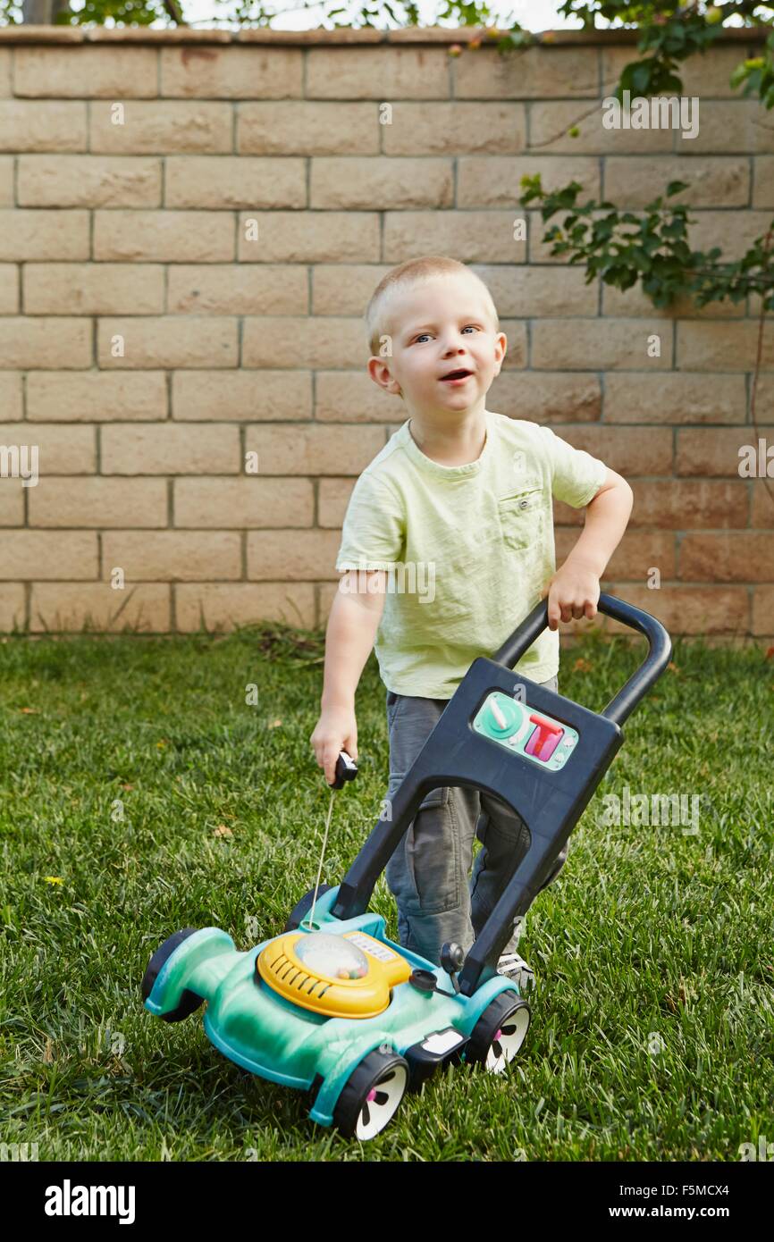 Boy playing with toy lawnmower in backyard Stock Photo