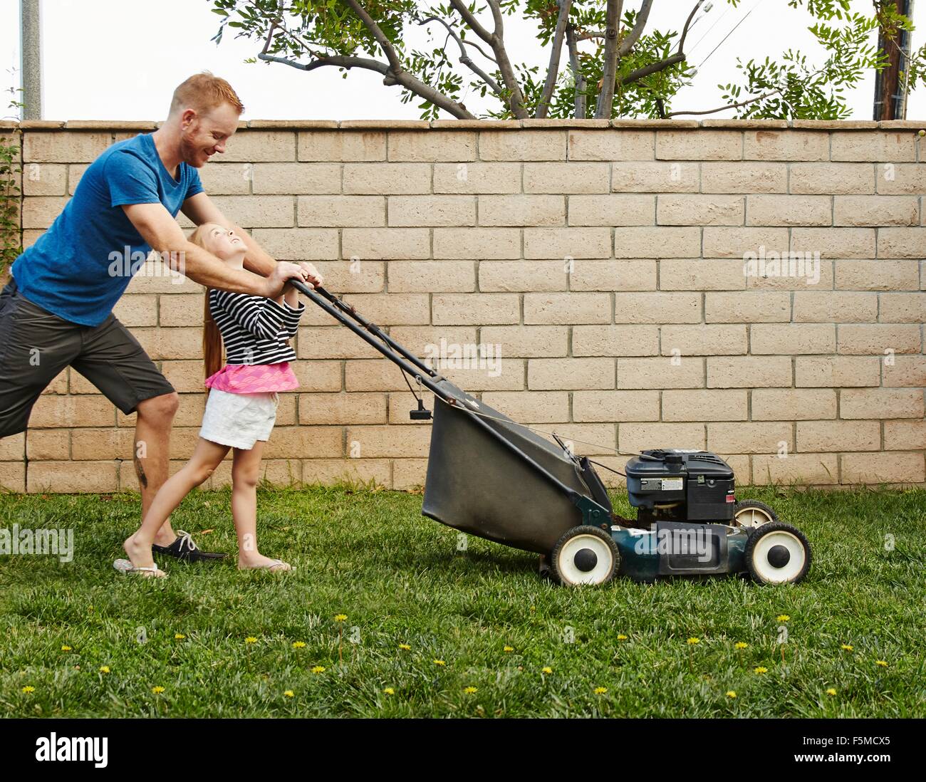 Father and daughter mowing lawn in backyard Stock Photo