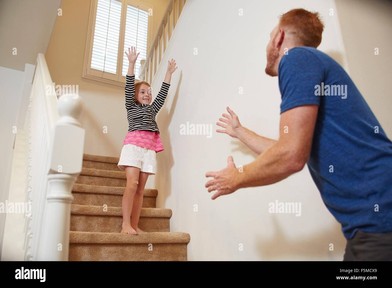 Girl preparing to jump into father's arms on staircase at home Stock Photo