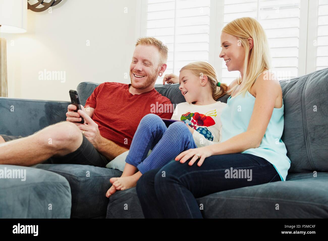Family chatting and using smartphone on sofa in living room Stock Photo