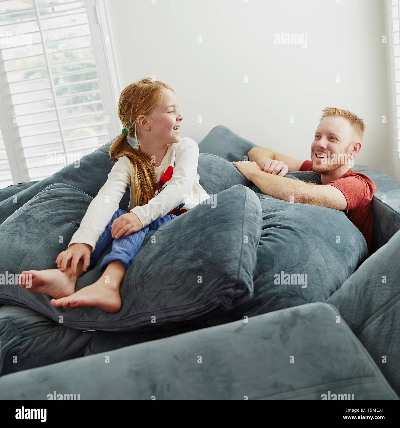Father and daughter playing on pile of cushions in living room Stock Photo