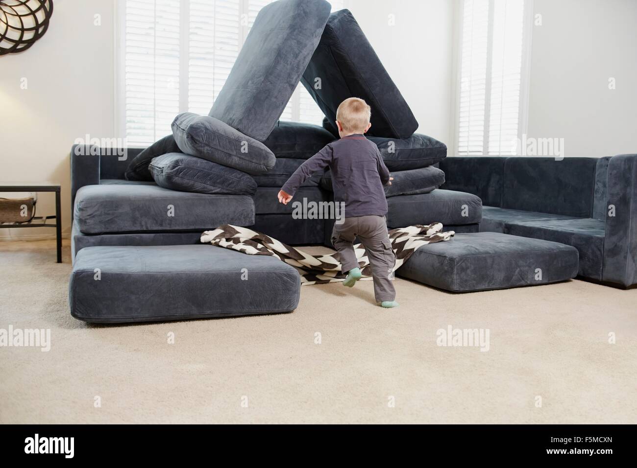 Boy running towards pile of cushions in living room Stock Photo