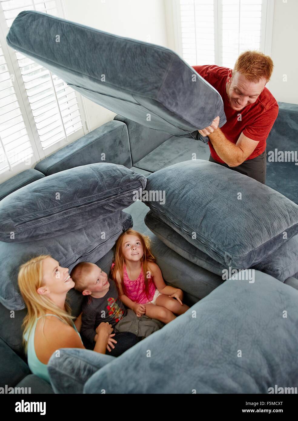 Father covering family sitting among cushions in living room Stock Photo