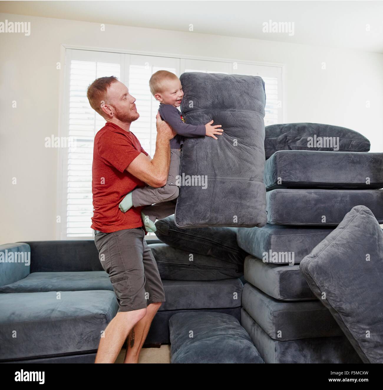 Father and son stacking cushions in living room Stock Photo