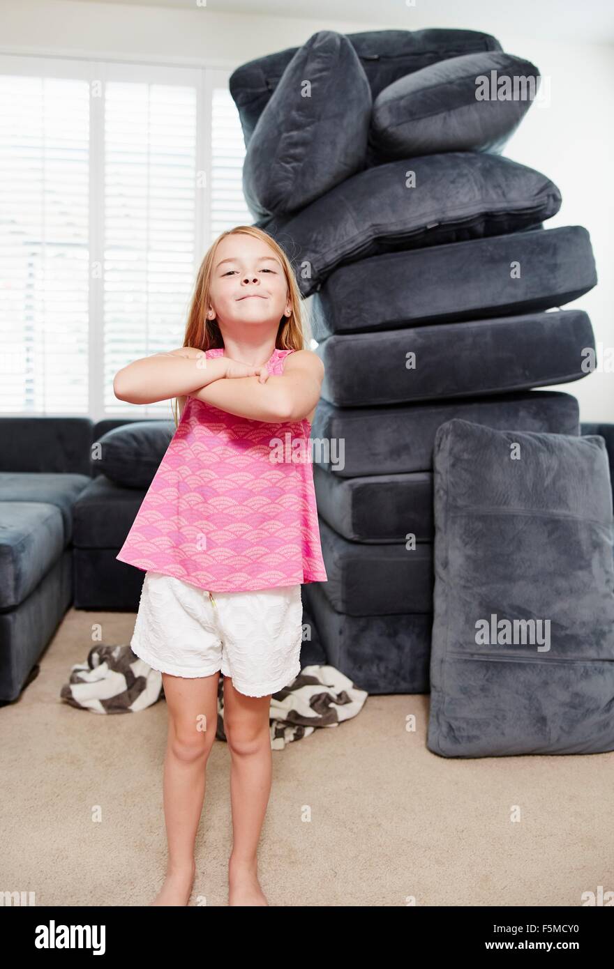 Girl with arms crossed in living room, pile of cushions in background Stock Photo