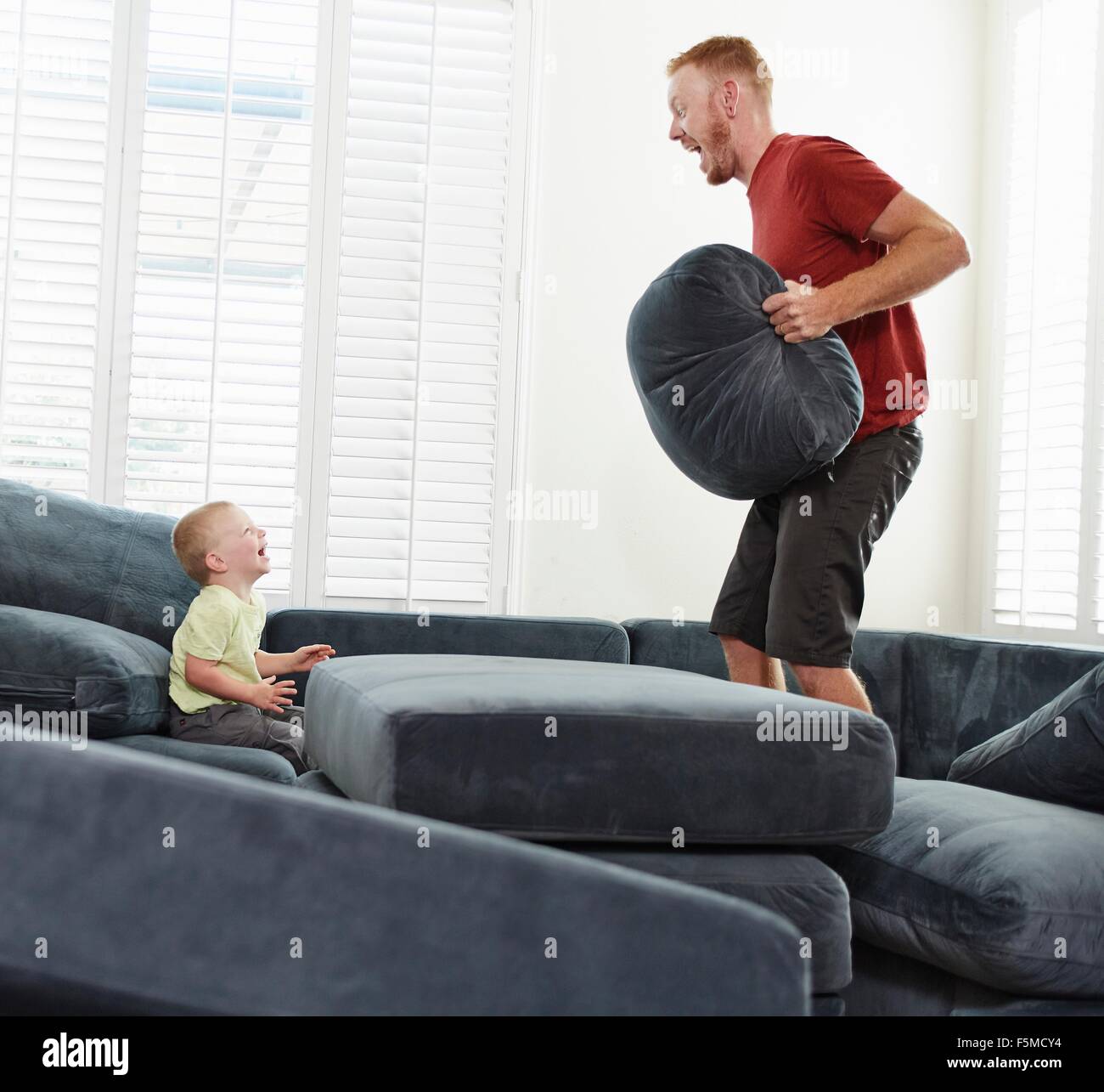 Father with pillow playing with son in living room Stock Photo