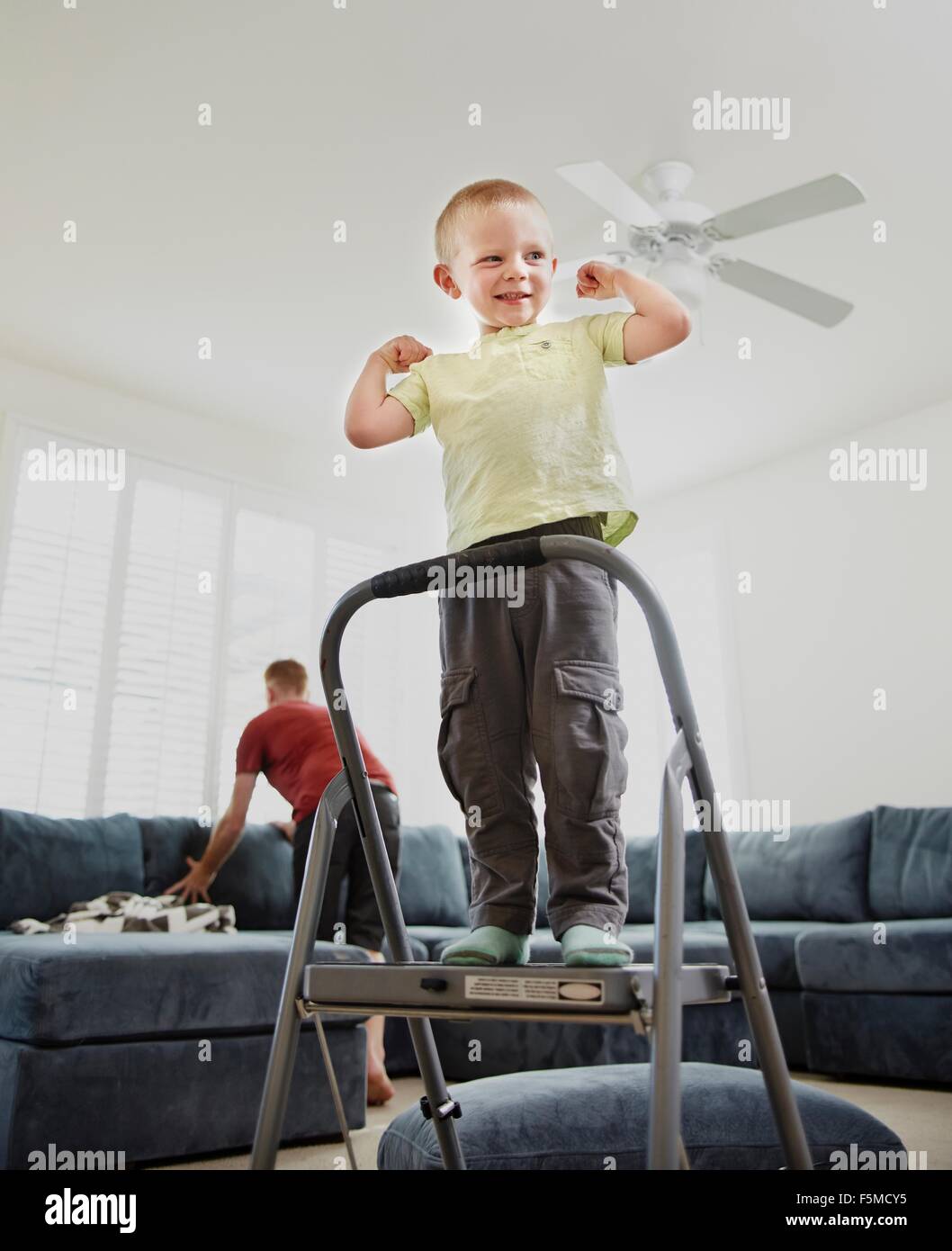 Boy flexing muscle in living room, father in background Stock Photo