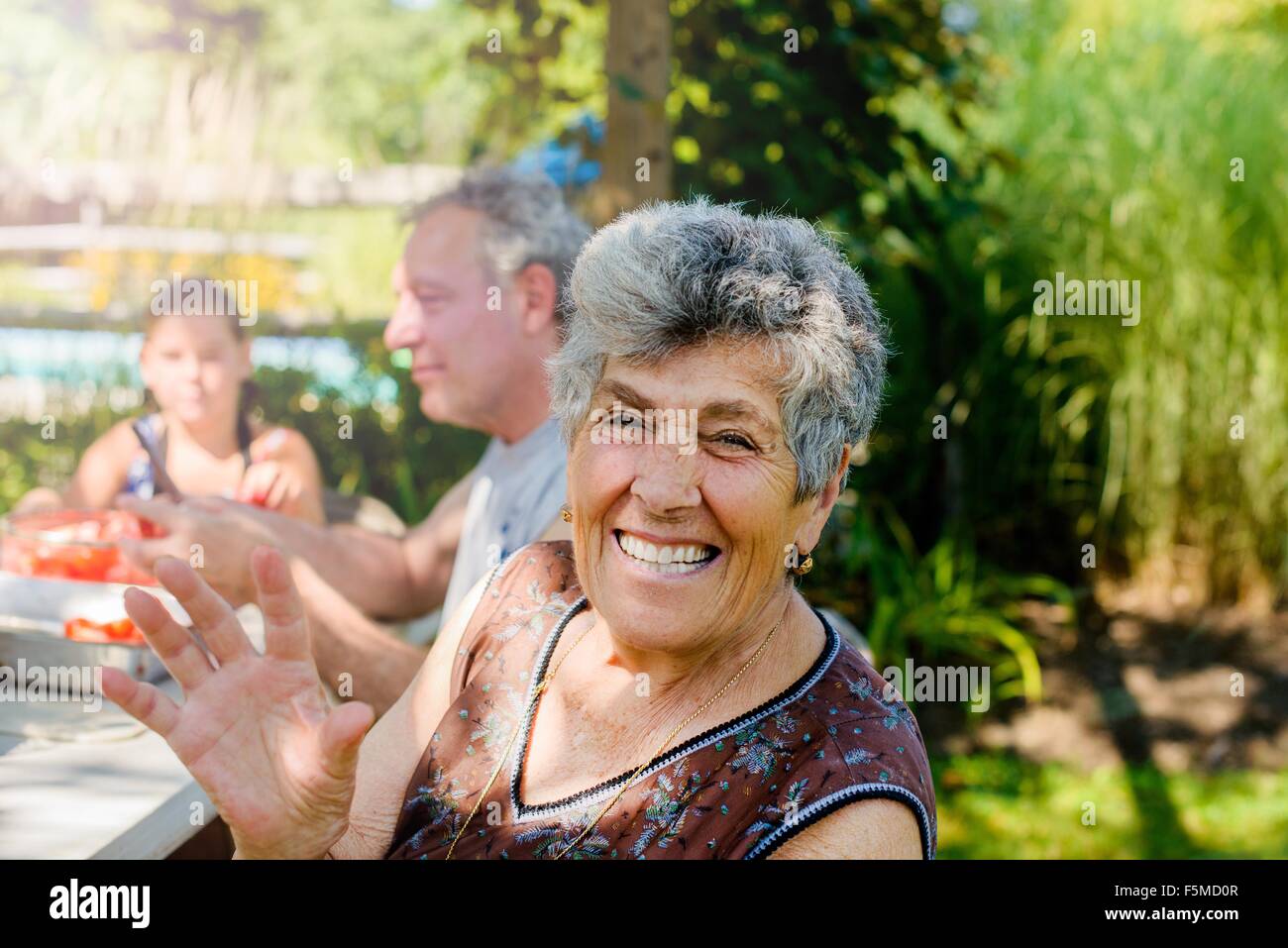 Senior woman outdoors with family looking at camera waving, smiling Stock Photo