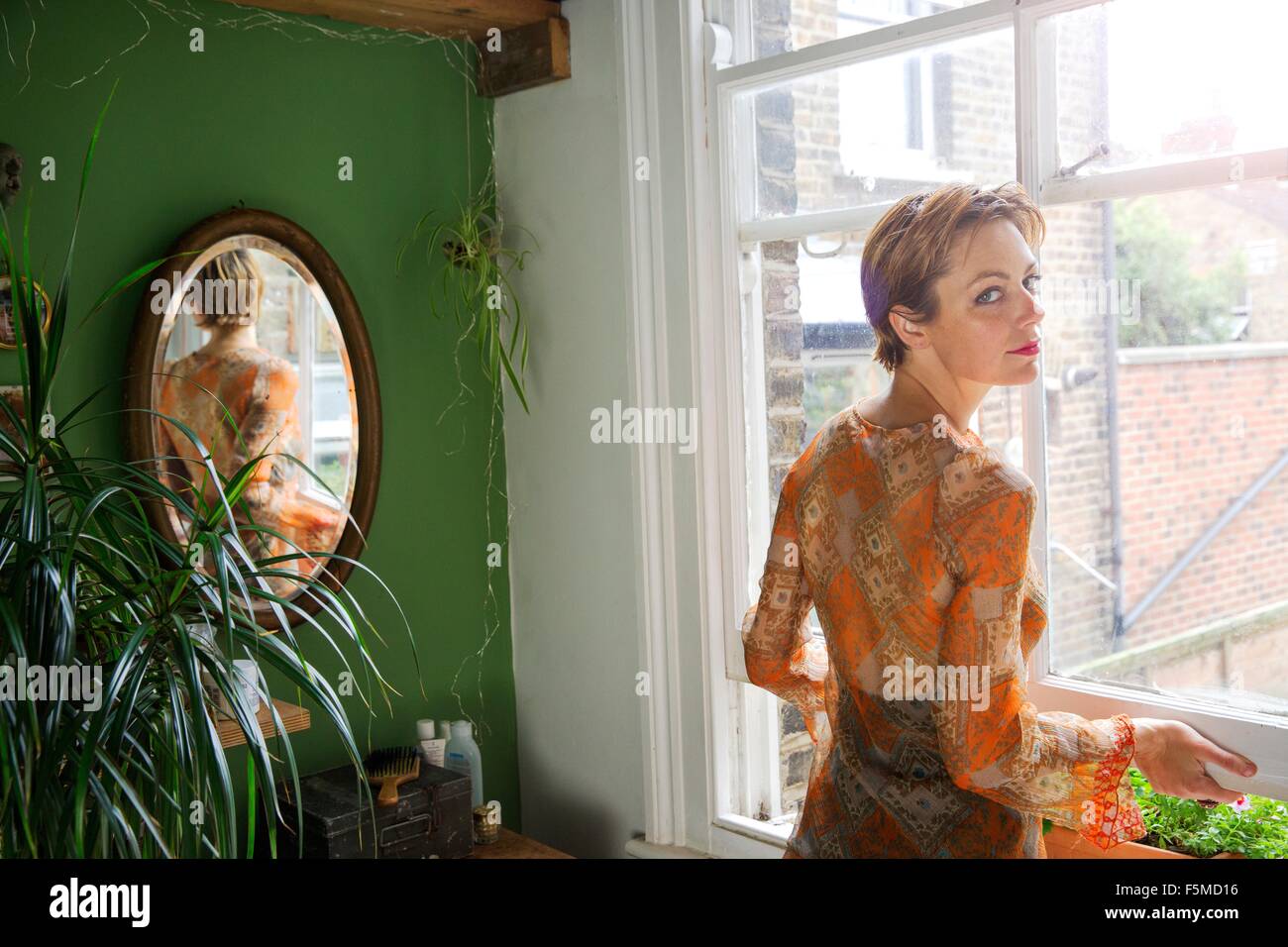 Portrait of mid adult woman looking over her shoulder whilst opening the window Stock Photo